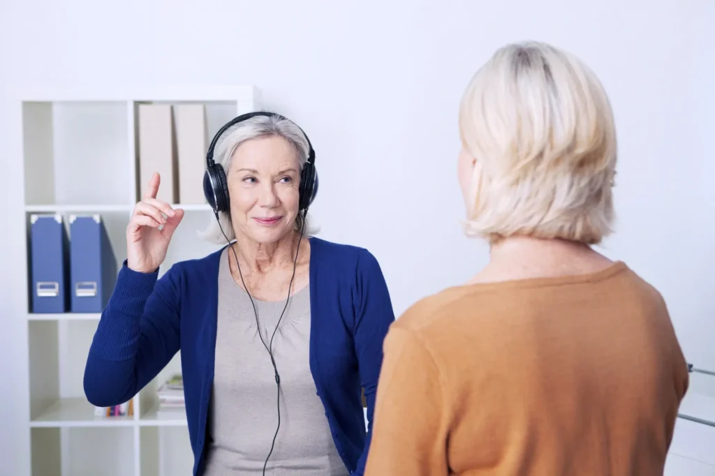 Woman over 50 raising hand during hearing assessment by Sound Hearing, illustrating early signs of hearing loss in a clinical setting