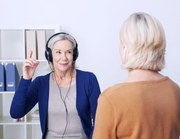 Woman over 50 raising hand during hearing assessment by Sound Hearing, illustrating early signs of hearing loss in a clinical setting